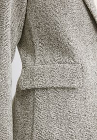 Grau kariertes Blazer im Hahnentrittmuster aus strukturiertem Wollmaterial, mit einer einzelnen Tasche und strukturiertem Revers.