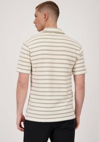 Polo de manga corta en color crema con rayas horizontales marrones. Cuenta con un cuello clásico y una tela texturada. Corte ajustado.