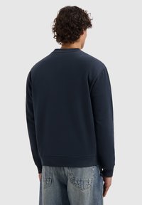 Marineblauwe sweatshirt met een ronde hals en geribbelde manchetten en onderkant. Gladde textuur, relaxte pasvorm en minimale details op de achterkant.