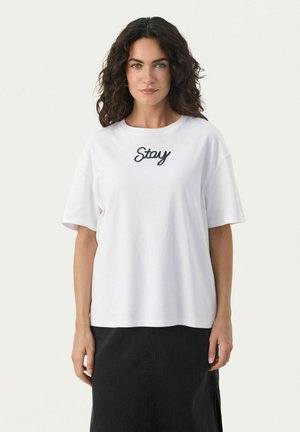 Camiseta de algodón blanca con mangas cortas, cuello redondo, que presenta "Stay" bordado en cursiva negra en el pecho.