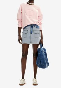Felpa rosa con logo in rilievo, mini gonna di jeans blu chiaro con tasche frontali e borsa di jeans blu. Sneakers bianche.