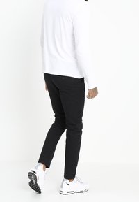 Musta kapealahkeiset farkut, joissa on takatasku, yhdistettynä valkoisiin lenkkareihin. Henkilö näkyy takaa kävelemässä.