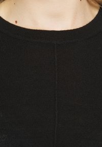 Tessuto a maglia nero con scollo rotondo e dettagli di cucitura sottili. La superficie appare morbida con un motivo leggermente in rilievo.
