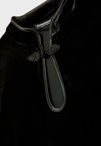 Sort velourbeklædning med ståkrave, der har en nøglehulåbning prydet med en dekorativ sort knude.