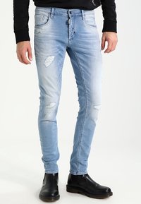 Bleknade ljusblå jeans med smal passform, med slitna lappar och subtila veck. Burit med svarta ankelskor.