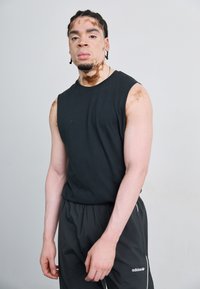 Tricou negru fără mâneci și pantaloni scurți atletici negri cu accente albe. Modelul are părul împletit până la umeri și variații vizibile ale pielii.