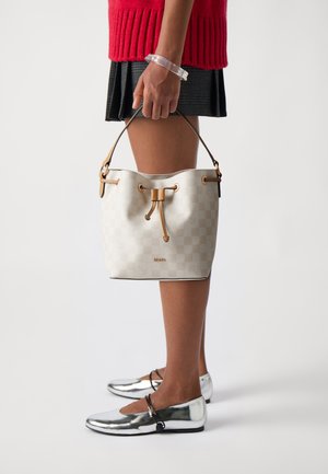 Sac seau à motif damier blanc avec des accents marron ; comporte une fermeture à cordon et une courte anse. Porté avec des ballerines argent métallisé.