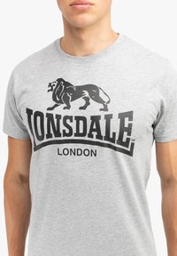 Siva pamučna majica s grafikom crnog lava i natpisom "Lonsdale London". Dizajn s okruglim izrezom, kratkim rukavima i mekim teksturom.