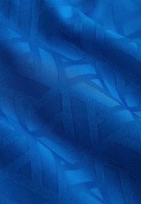 Tissu bleu avec un motif géométrique subtil composé de formes triangulaires et linéaires entrelacées aux textures variées.