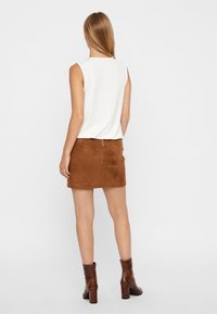 Haut blanc sans manches associé à une mini-jupe en daim marron. Bottines marron à finition texturée. Vue de dos de la tenue.