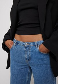 Augstās jostas vietas zilas džinsu bikses ar nolietotu tekstūru, piecām kabatām un sudraba pogu aizdari. Apvienotas ar melnu ribotu topi un žaketi.