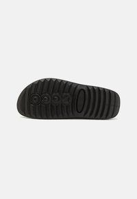 Suola di scarpa in gomma nera con texture rigata, dotata di accenti a logo circolare e un'apertura ovale. Design piatto e ampia per stabilità.