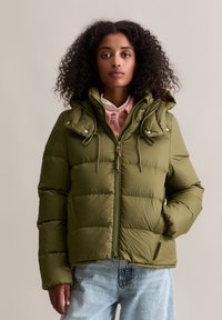 Oliwkowa kurtka puchowa z zamek błyskawicznym z przodu, regulowanym kapturem ze sznurkiem i dwoma kieszeniami na piersi. Charakteryzuje się pikowanym wzorem i miękką teksturą.