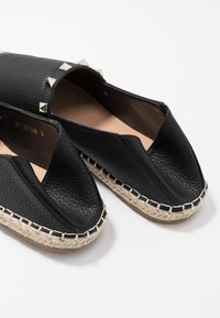 Espadrilles en cuir noir avec une finition texturée, ornées de clous en pyramide métallique sur le dessus et d'une semelle en jute naturel avec des détails de couture.