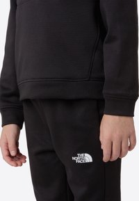 Musta collegepaita ja housut, valmistettu pehmeästä kankaasta. Housuissa valkoinen logo. Yksinkertainen muotoilu ja rento istuvuus.