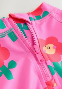 Costume da bagno rosa con motivi floreali, foglie verdi e una cerniera rosa. Materiale morbido e elasticizzato con una texture liscia.