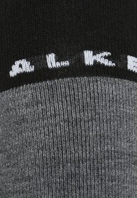 Czarna i szara skarpetka z prążkowaną teksturą. Górny pas zdobi biały napis. Dolna część ma jednolicie szary kolor o gładkim wykończeniu.