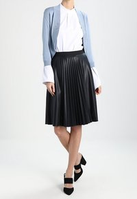 Ljusblå kardin över en vit topp, i kombination med en svart plisserad fusk läderkjol. Svarta klackar med blockklackar fulländar outfiten.