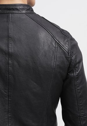 Homme portant une veste en cuir noire vue de dos, mettant en avant la surface texturée de la veste et les coutures cousues.