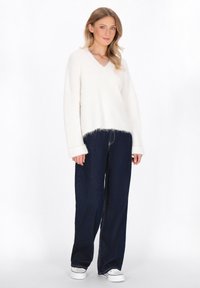 Biały, puszysty sweter v-neck o luźnym kroju, zestawiony z ciemnoniebieskimi spodniami o szerokich nogawkach i białymi sneakerami. Teksturowana tkanina z prążkowanymi detalami.