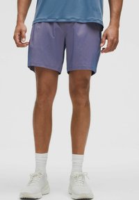Lilla atletiske shorts med en glat tekstur og en elastisk talje, suppleret med en blå skjorte og hvide sneakers.