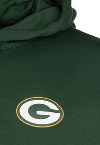 Sudadera verde con bolsillo canguro. Presenta un logo blanco y amarillo con la letra "G" en el pecho. Tela suave, corte relajado, superficie texturizada.