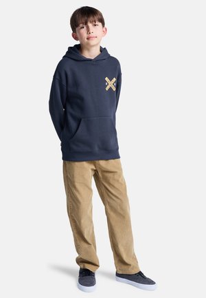Marineblauwe hoodie met een voorzak en een grafisch ontwerp op de borst, gecombineerd met khaki ribfluwelen broek en donkere sneakers.