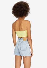 Top sin tirantes amarillo y pantalones cortos de denim azul claro, con un dobladillo desgastado y dos bolsillos traseros, con una etiqueta visible en la cinturilla.