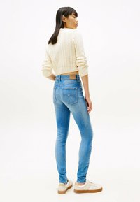 Jeans skinny de denim azul claro con una subida media, bolsillos traseros y una etiqueta de cuero beige en la cintura. Combinados con un suéter corto de punto trenzado en color crema.