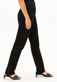 Pantalon en denim noir avec une coupe droite, doté de deux poches avant et de deux poches arrière, associé à des chaussures à talons ouverts noires.