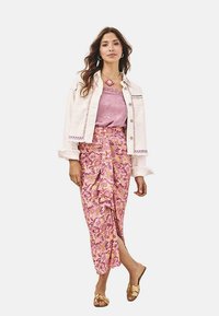 Chaqueta blanca corta con bordado, llevada sobre una blusa de satén rosa y una falda rosa con patrón, combinada con sandalias doradas.