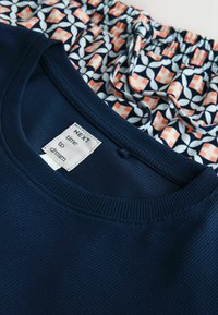 Marineblauw geribd T-shirt met een ronde hals en een kledinglabel, gecombineerd met patroonshorts met marineblauwe, perzik- en witte geometrische ontwerpen.