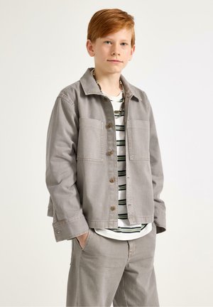 Grå denimjakke med to forlommer, knappelukning og en afslappet pasform, lagdelt over en stribet T-shirt, kombineret med matchende bukser.