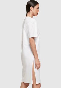Biała bawełniana sukienka t-shirtowa z krótkimi rękawami, bocznymi rozcięciami i luźnym krojem, sięgająca do połowy uda. Gładka tekstura i prosty design.