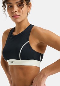Black athletic crop top with a white band featuring "ROXY" logo, curved seams, and a seamless design for added comfort.
