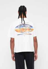 T-shirt branca com um gráfico redondo que representa um mapa-múndi e uma escala de temperatura em laranja e azul. Corte relaxado, mangas curtas.