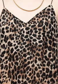 Top imprimé léopard à col en V avec fines bretelles noires et collier chaîne dorée torsadée sur un fond de teint clair.