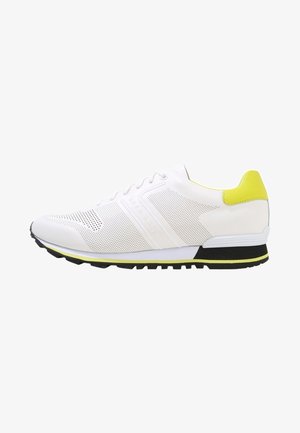 Biały sportowy sneaker z perforowanymi bokami, żółtą zakładką na pięcie, czarno-żółtą podeszwą oraz oznaczeniem "Hugo Boss" z boku.