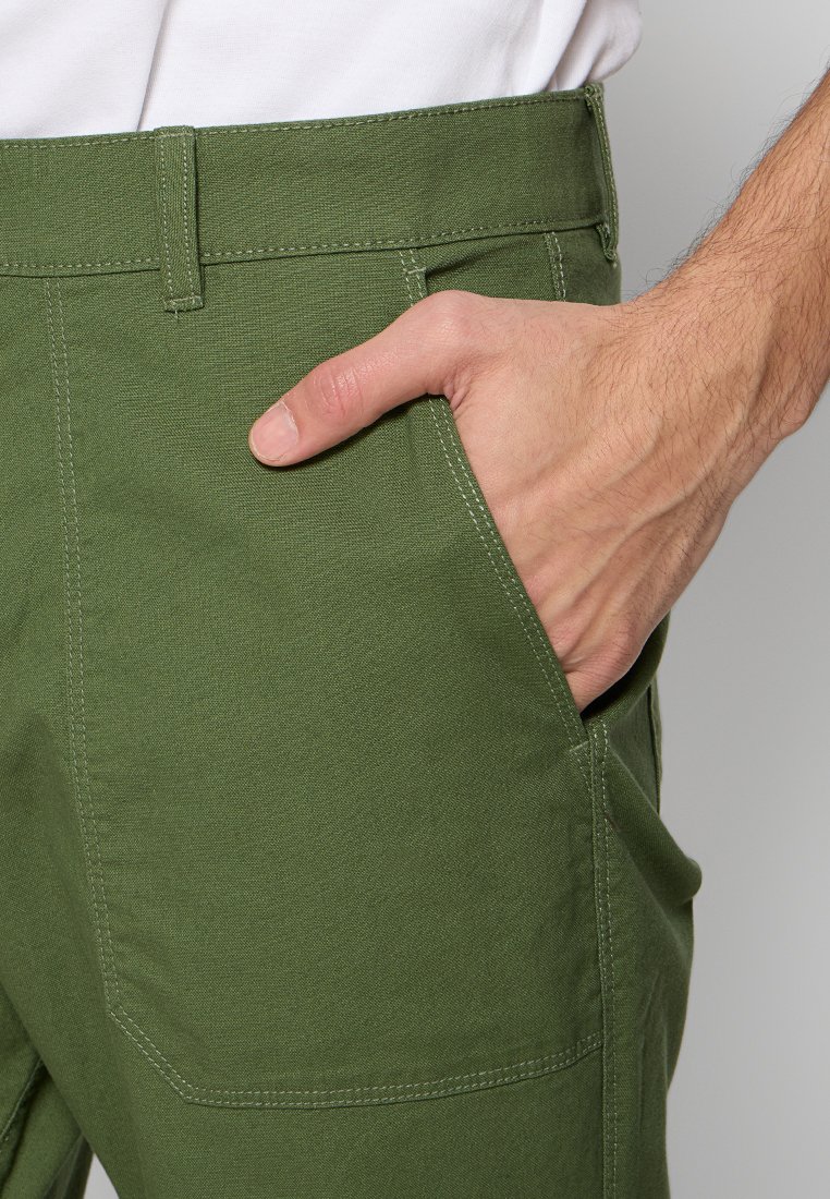 Grüne Baumwollhosen mit geradem Schnitt, ausgestattet mit seitlichen Taschen und sichtbaren Nähten. Der Stoff hat eine strukturierte Oberfläche.