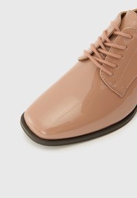 Patent leather dress shoe in a light pink hue, featuring a pointed toe, matching laces, and a contrasting black sole.