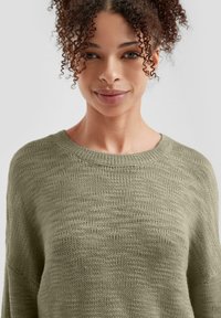 Olivengrüner Strickpullover mit weitem Ausschnitt und texturiertem Stoff. Lange Ärmel und eine lockere Passform mit minimaler Ausstattung.