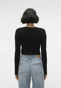 Črn rebrast dolg rokav vrh, nosen z visokim pasom svetlo modrih jeans hlač, ki imajo usnjeni našitek na pasu in zadnjih žepih.