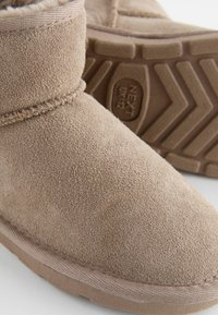 Beige Wildleder-Ankle-Boots mit runder Zehenform, strukturiertem Obermaterial und weicher Innenausstattung. Sie verfügen über eine gummierte Sohle mit Profil für besseren Halt.
