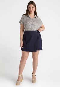 Blusa de manga corta con cuello y estampado geométrico en tonos blanco, marino y dorado; combinada con una falda tipo wrap en color marino con un detalle de costura roja.