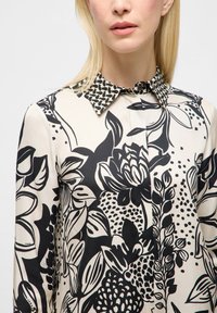 Blusa floreale con motivi botanici in bianco e nero, con un colletto a fantasia a contrasto, realizzata in tessuto leggero.