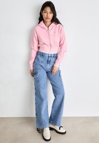 Rosa crop hoodie med glidelås, høy midje lyseblå cargojeans og beige loafers med svarte såler. Enkel, uformell gateklesestetikk.
