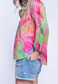 Värikäs, kevyt paita, jossa on eläväinen vaaleanpunaisen, vihreän ja keltaisen palmulehtikuvio; siinä on pitkät, puhditut hihat ja löysä istuvuus.