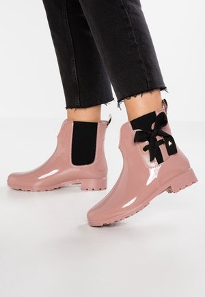 Skinnende lyserøde ankelregnstøvler med sorte elastiske sidepaneler og sorte snørebånd, båret med afklippede sorte jeans med frynser.