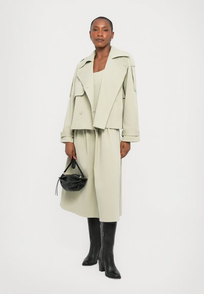 Light green oversized jacket with wide lapels, paired with a matching dress. Black leather handbag and knee-high black heeled boots.