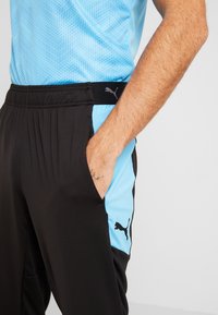 Schwarze Sporthose mit blauen Seitenpaneelen, einem strukturierten schwarzen Bund mit Logo und Seitentaschen für Funktionalität.